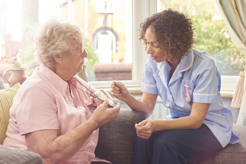 elderly woman and a health visitor use mobile working technology, like a fall sensor