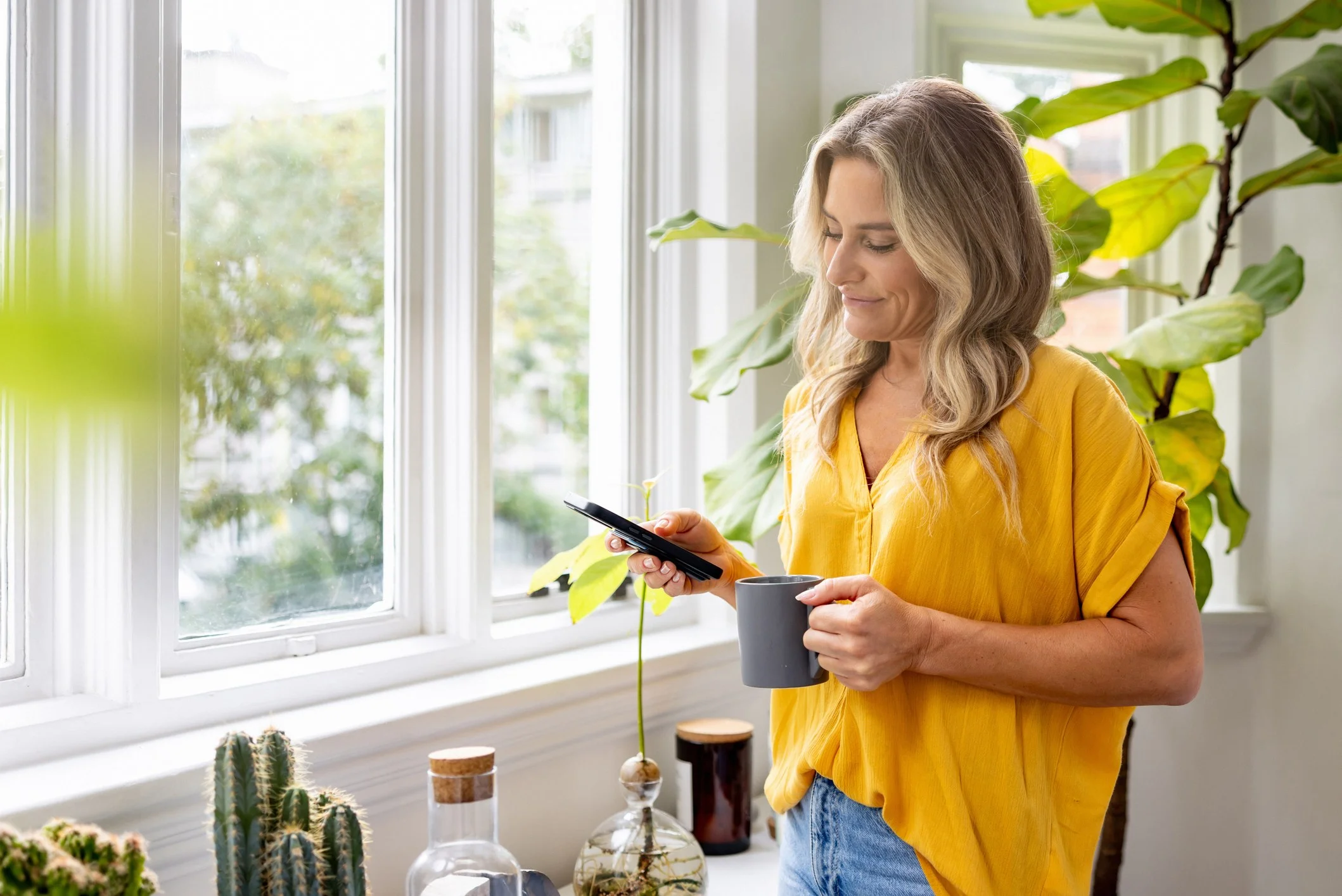 Woman in yellow shirt, holding a cup and on her phone