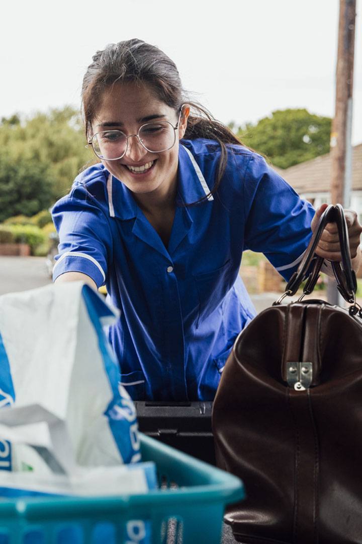 Mobile care worker lifting prescription bag from car rear opening.