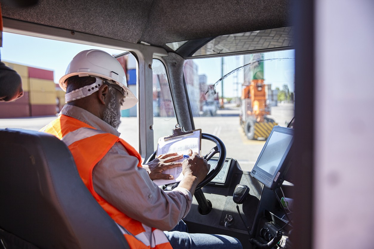 Delivery driver wearing bright orange PPE handles device routing smart schedule.