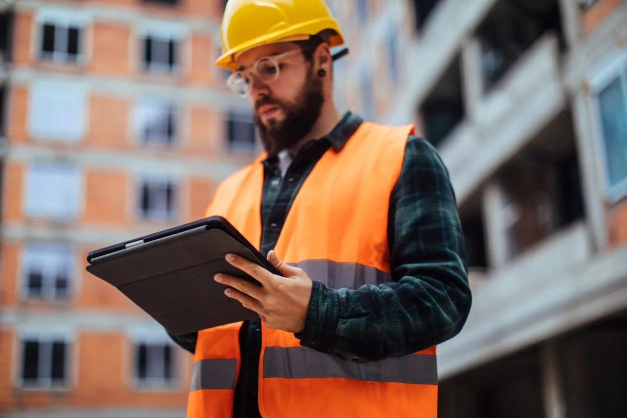 Male service engineer in hi-vis PPE in apartment courtyard holding tablet PC.