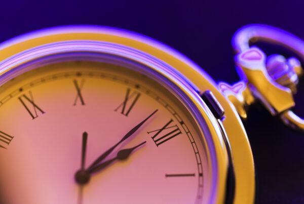 Roman numeral stopwatch on modern purple and orange background, used as hero image for rota vs. roster blog.