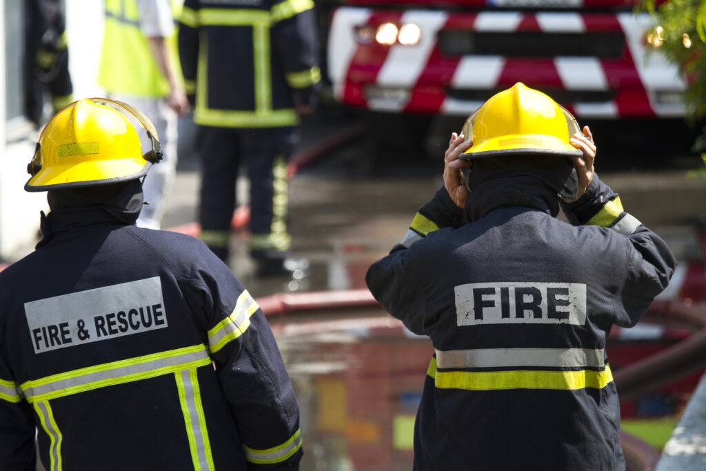 2 firefighters at work, facing forward, each wearing a yellow hat and protective gear