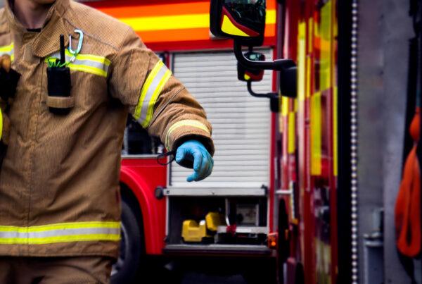 A fireman holding their yellow helmet by the firetruck