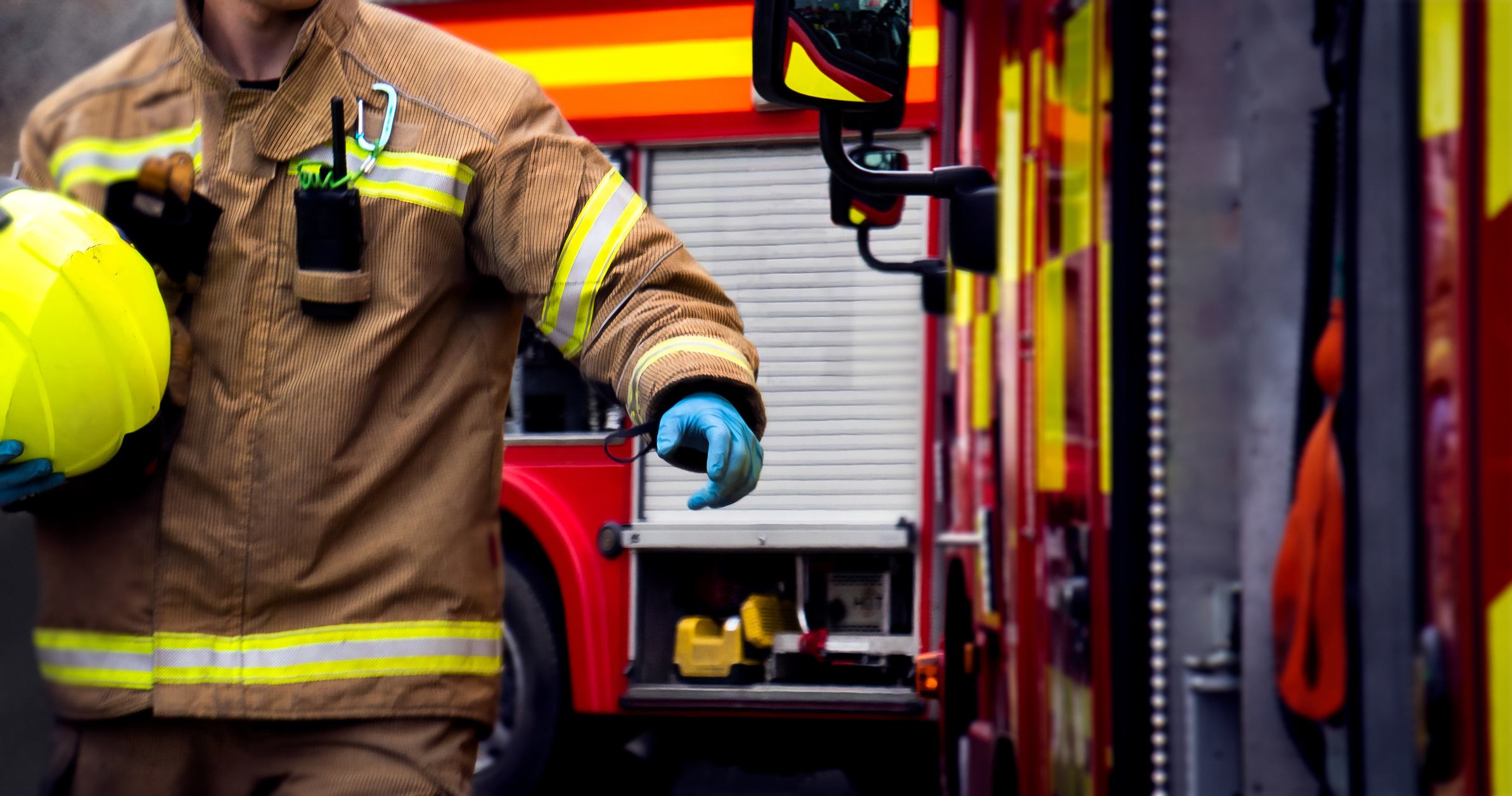 A fireman holding their yellow helmet by the firetruck