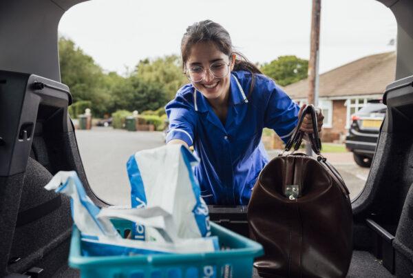 Young female care worker arriving at service user property reaching in to car boot to lift bag